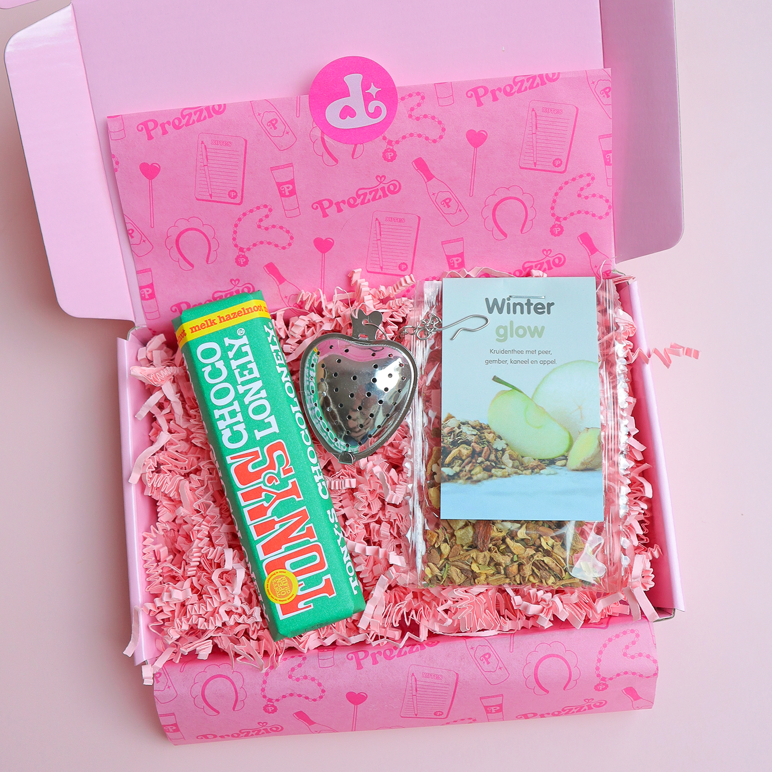 Brievenbuscadeau met Winter Glow thee, mini Tony’s Chocolonely reep en zilveren aardbei-theezeef in roze Prezzie verpakking.