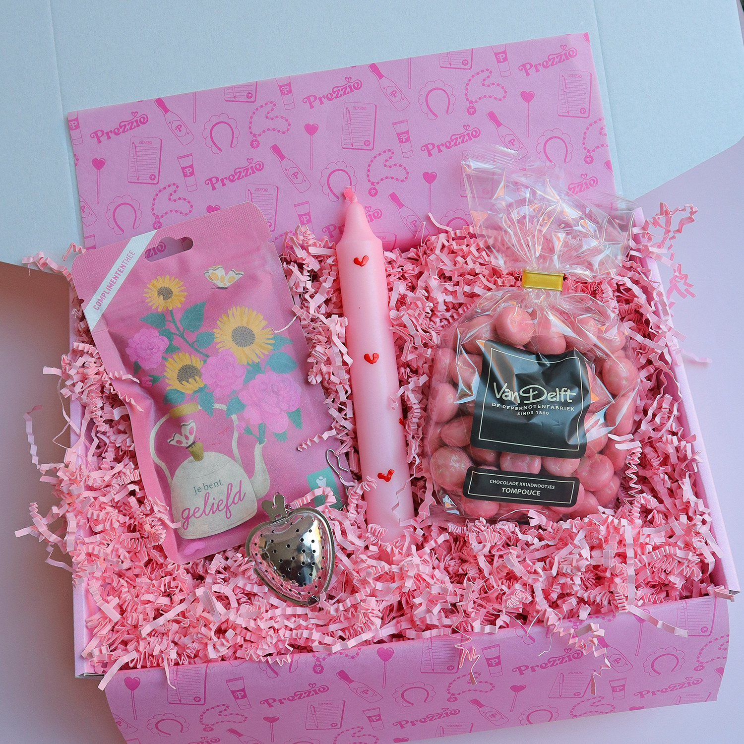 Liefdevol cadeaupakket met roze hartjeskaars, tompouce kruidnoten, thee en theehanger in roze Prezzie verpakking.