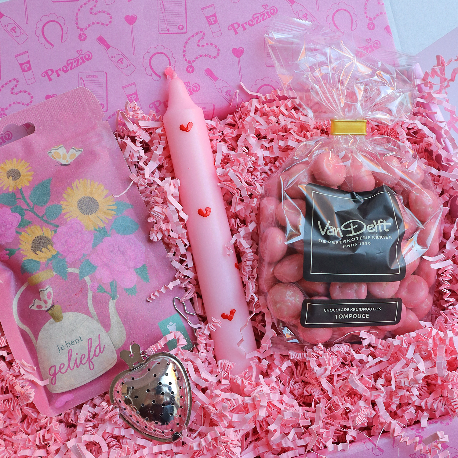 Liefdevol cadeaupakket met roze hartjeskaars, tompouce kruidnoten, thee en theehanger in roze Prezzie verpakking.